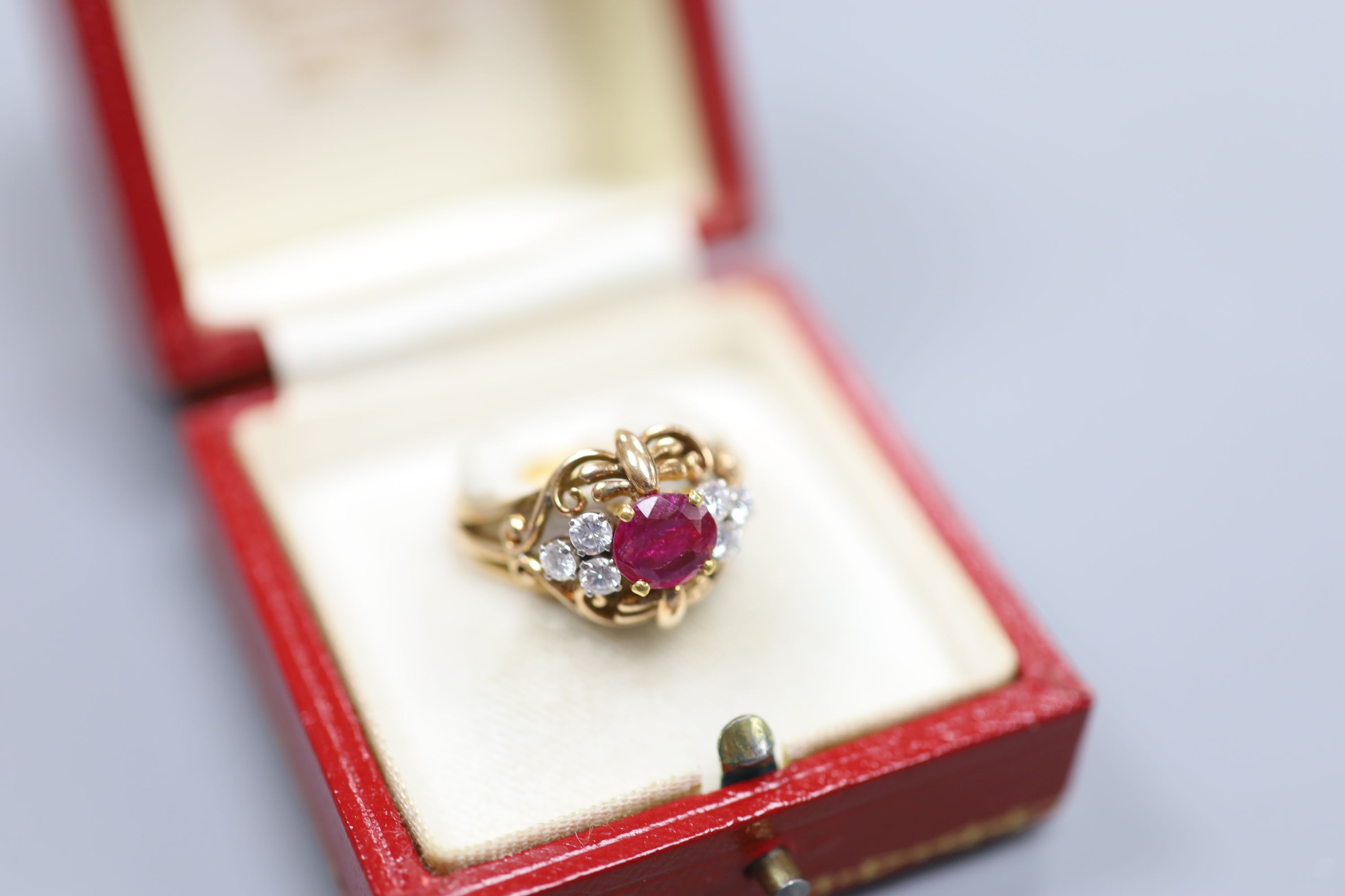 A stylish yellow metal, ruby and diamond set cluster ring, with single round cut ruby(crack), flanked by six round cut diamonds, in an openwork scroll setting, size Q/R, gross weight 7.5 grams, in a Cartier box.